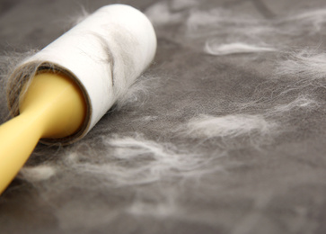 Modern lint roller and cat hair on brown fabric, closeup