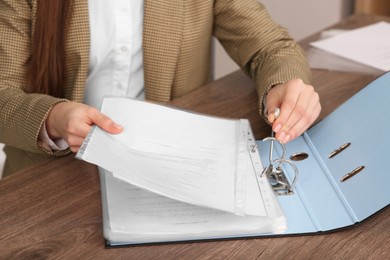 Businesswoman putting document into file folder at wooden table in office, closeup
