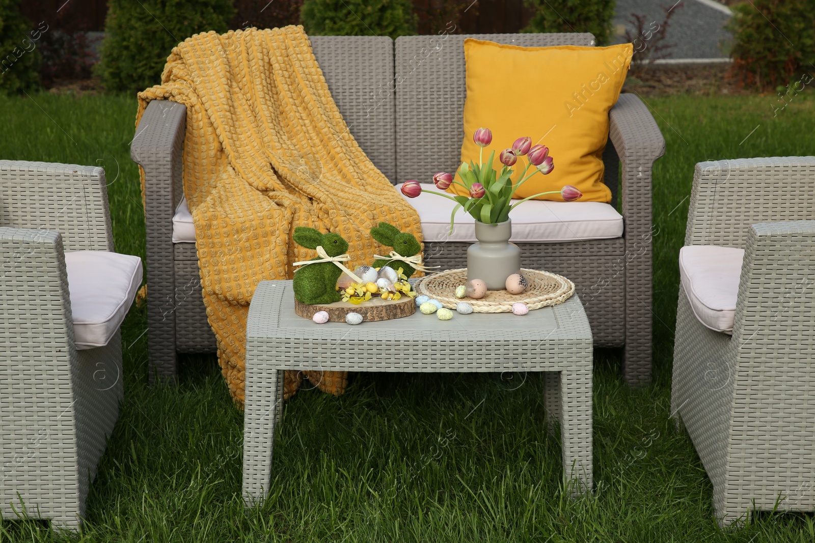 Photo of Easter decorations. Bouquet of tulips in vase, bunny figures and decorated eggs on table in backyard