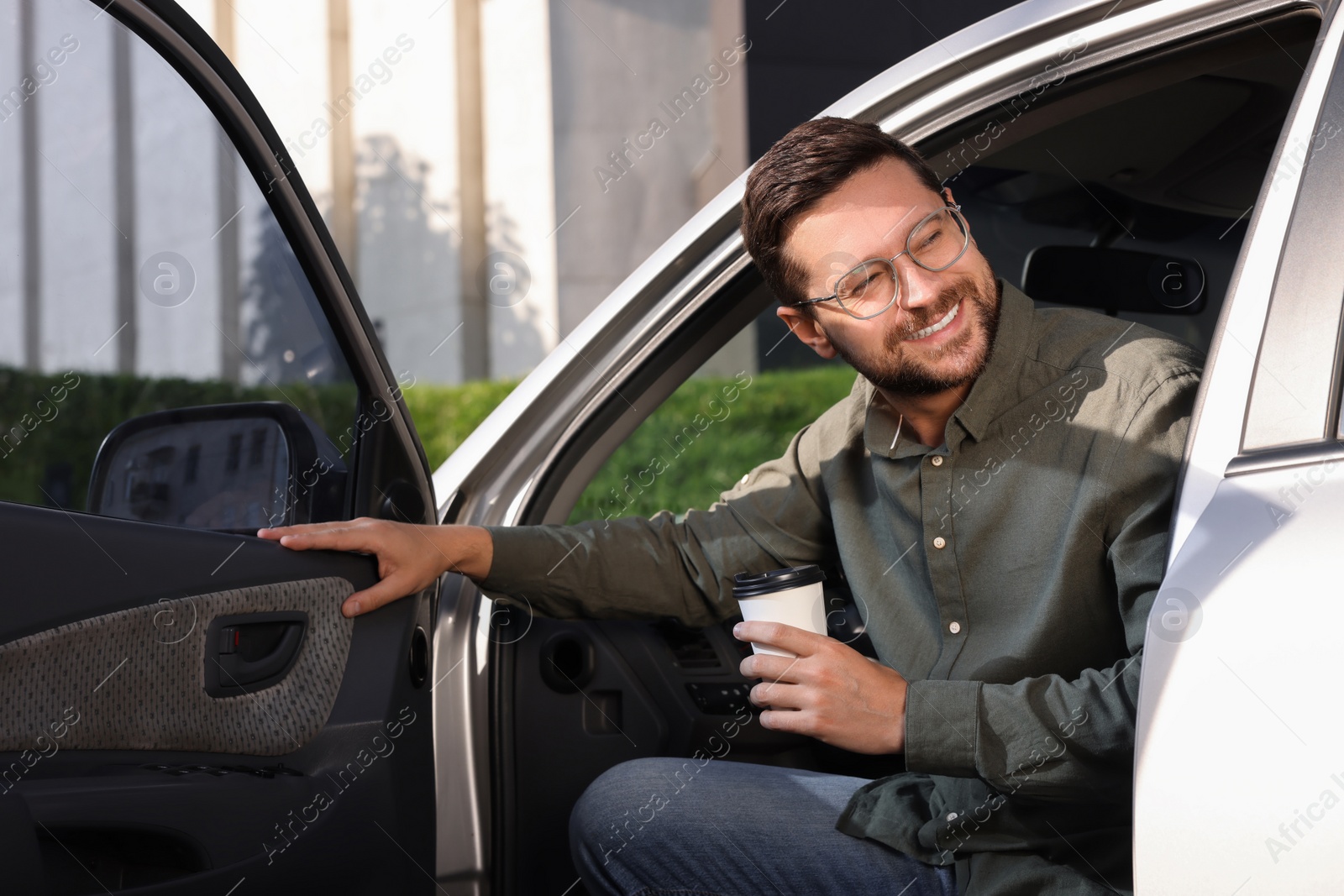 Photo of Coffee to go. Happy man with paper cup of drink in car outdoors