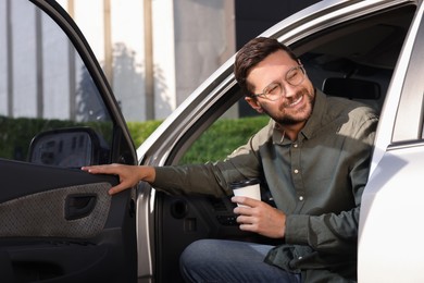 Coffee to go. Happy man with paper cup of drink in car outdoors