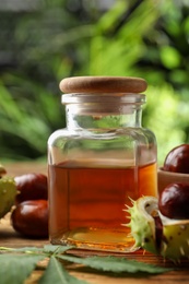 Photo of Chestnuts and jar of essential oil on table against blurred background