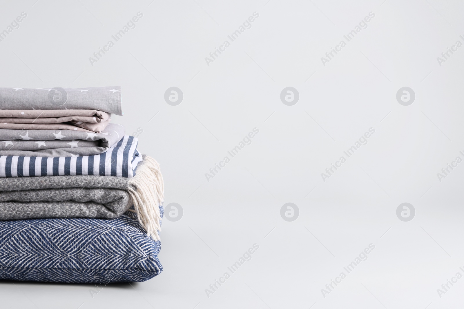 Photo of Stack of clean bed sheets and pillow on white background. Space for text