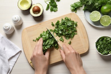 Photo of Woman cutting fresh green cilantro at white wooden table, top view