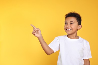 Photo of Cute African-American boy pointing on yellow background. Space for text