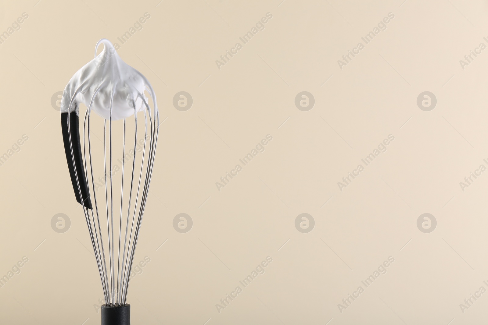 Photo of Whisk with whipped cream on beige background. Space for text