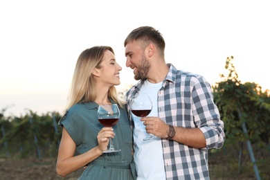 Young romantic couple holding glasses of wine at vineyard