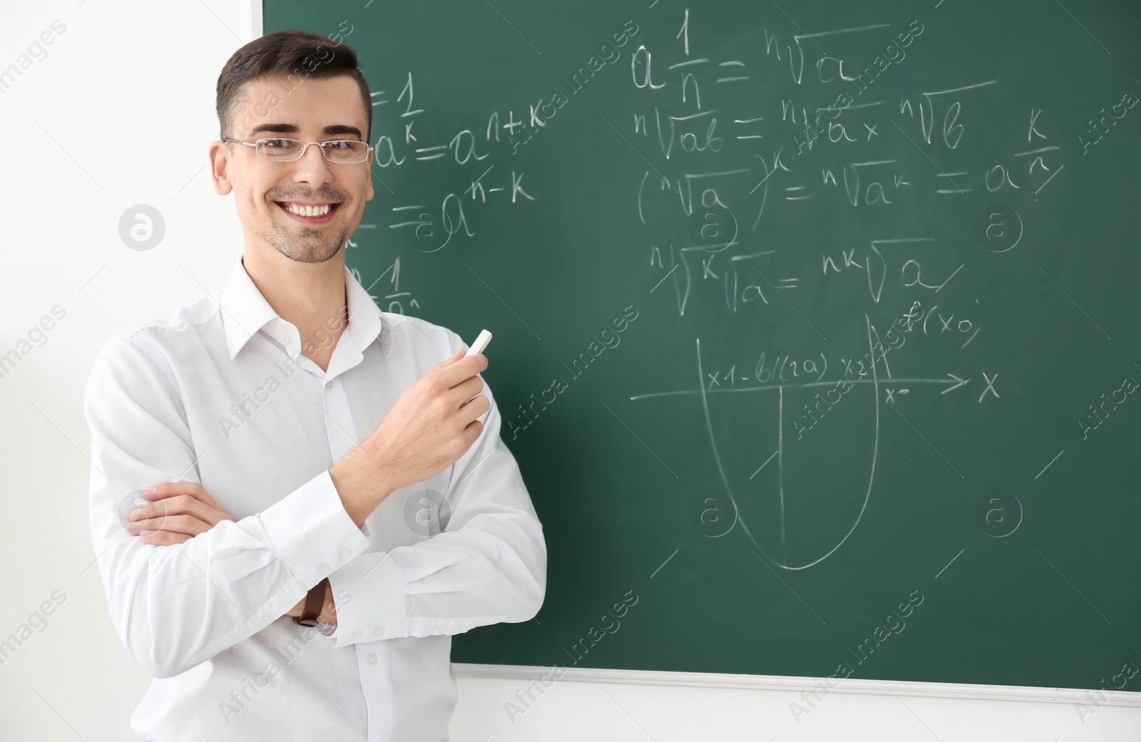 Photo of Young male teacher with chalk near blackboard in classroom