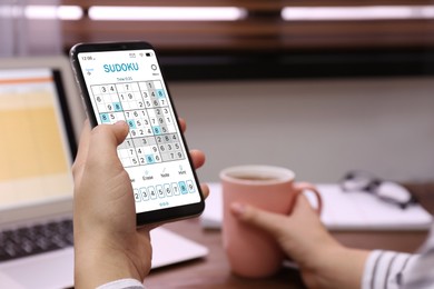 Image of Woman playing sudoku game on smartphone indoors, closeup