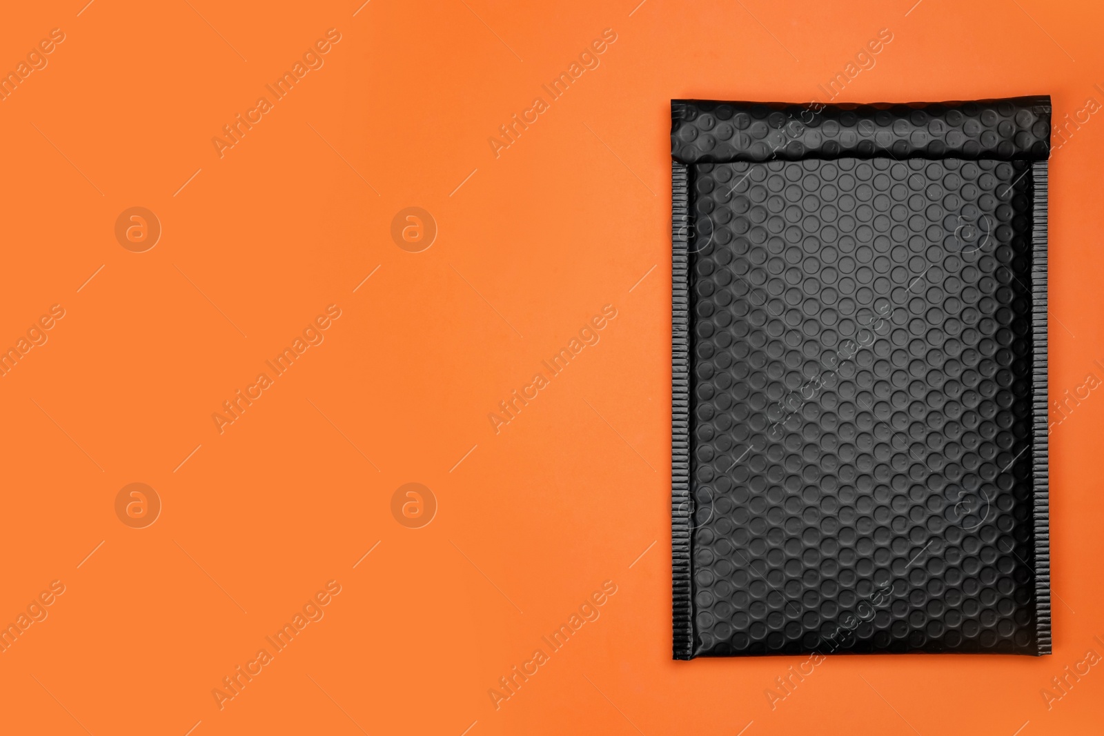 Photo of Padded envelope with bubble wrap on orange background, top view. Space for text