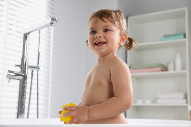 Photo of Happy little girl with toy in bathtub at home
