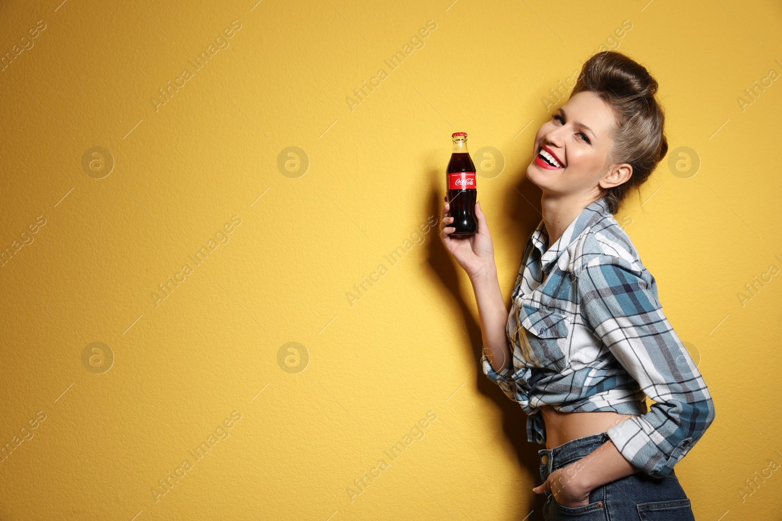 Photo of MYKOLAIV, UKRAINE - NOVEMBER 28, 2018: Young woman with bottle of Coca-Cola on color background, space for text