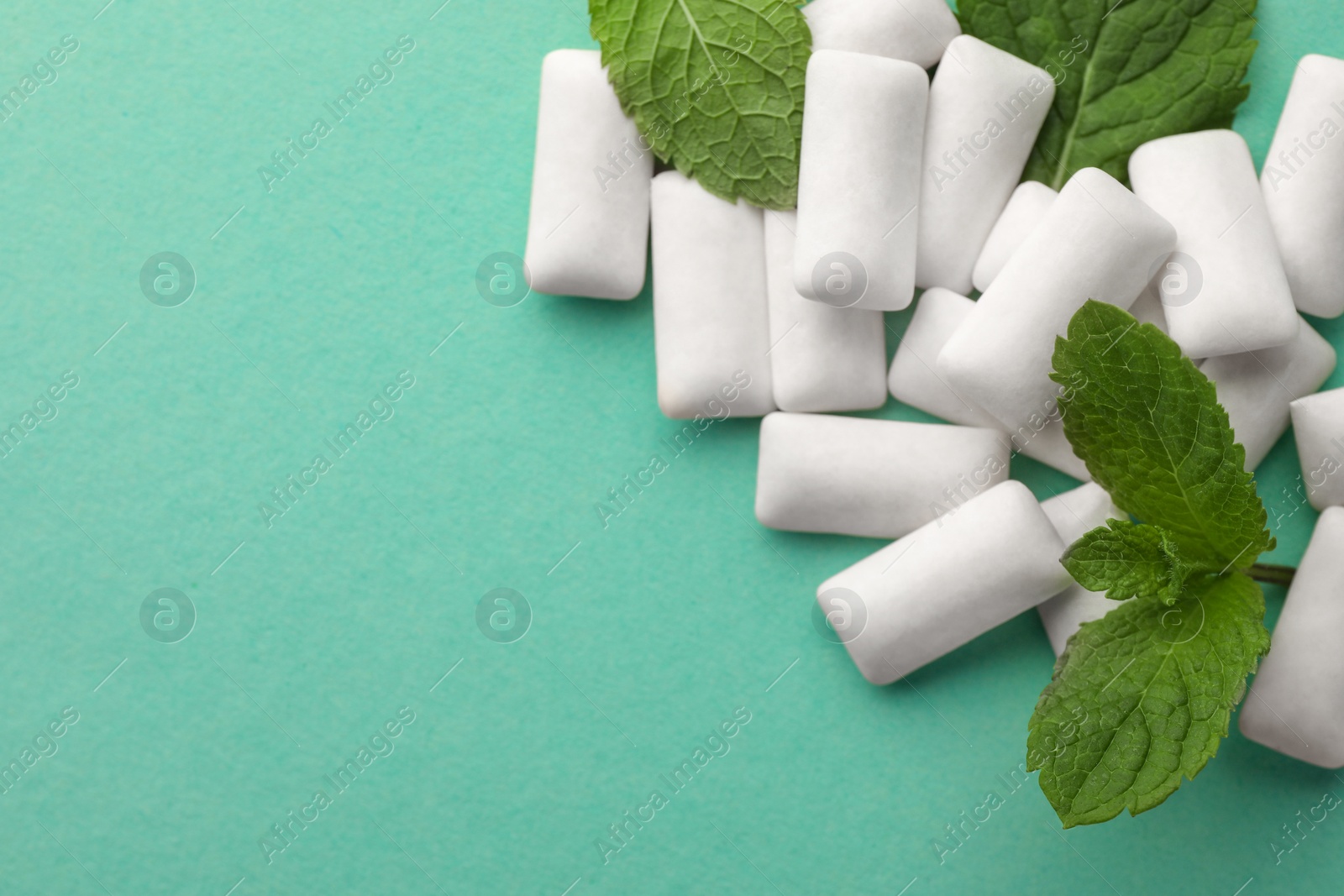 Photo of Tasty white chewing gums and mint leaves on turquoise background, above view. Space for text