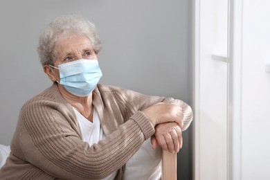 Photo of Lonely senior woman in protective mask sitting on bed at nursing home