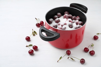 Photo of Pot with cherries and sugar on white wooden table. Making delicious jam