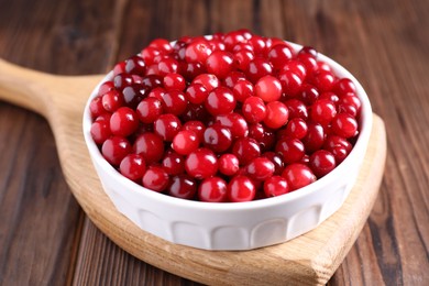 Photo of Fresh ripe cranberries in bowl on wooden table, closeup