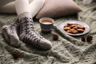 Photo of Woman wearing warm socks on knitted plaid, closeup. Cozy season