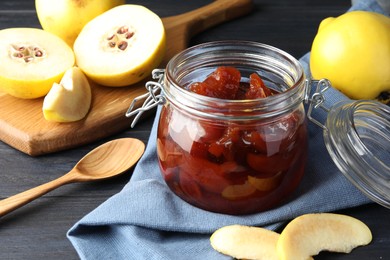 Photo of Quince jam in glass jar, spoon and fresh raw fruits on grey table, closeup