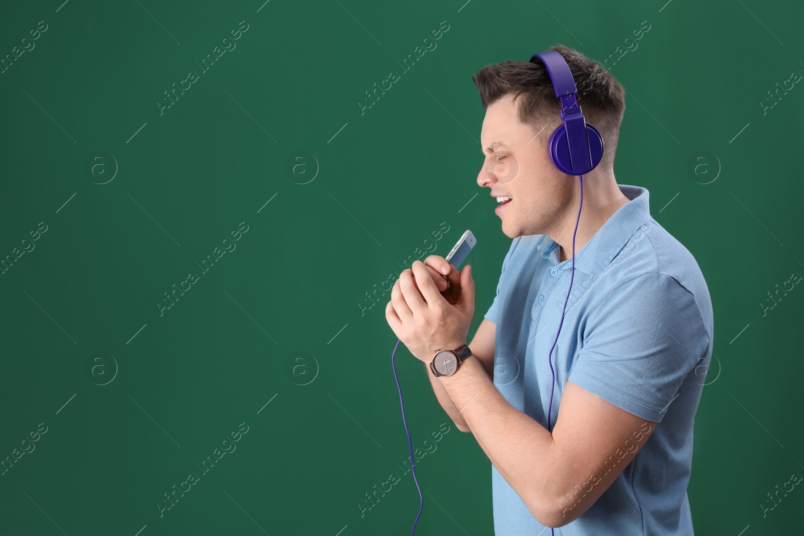 Photo of Man in headphones with mobile device on color background. Space for text