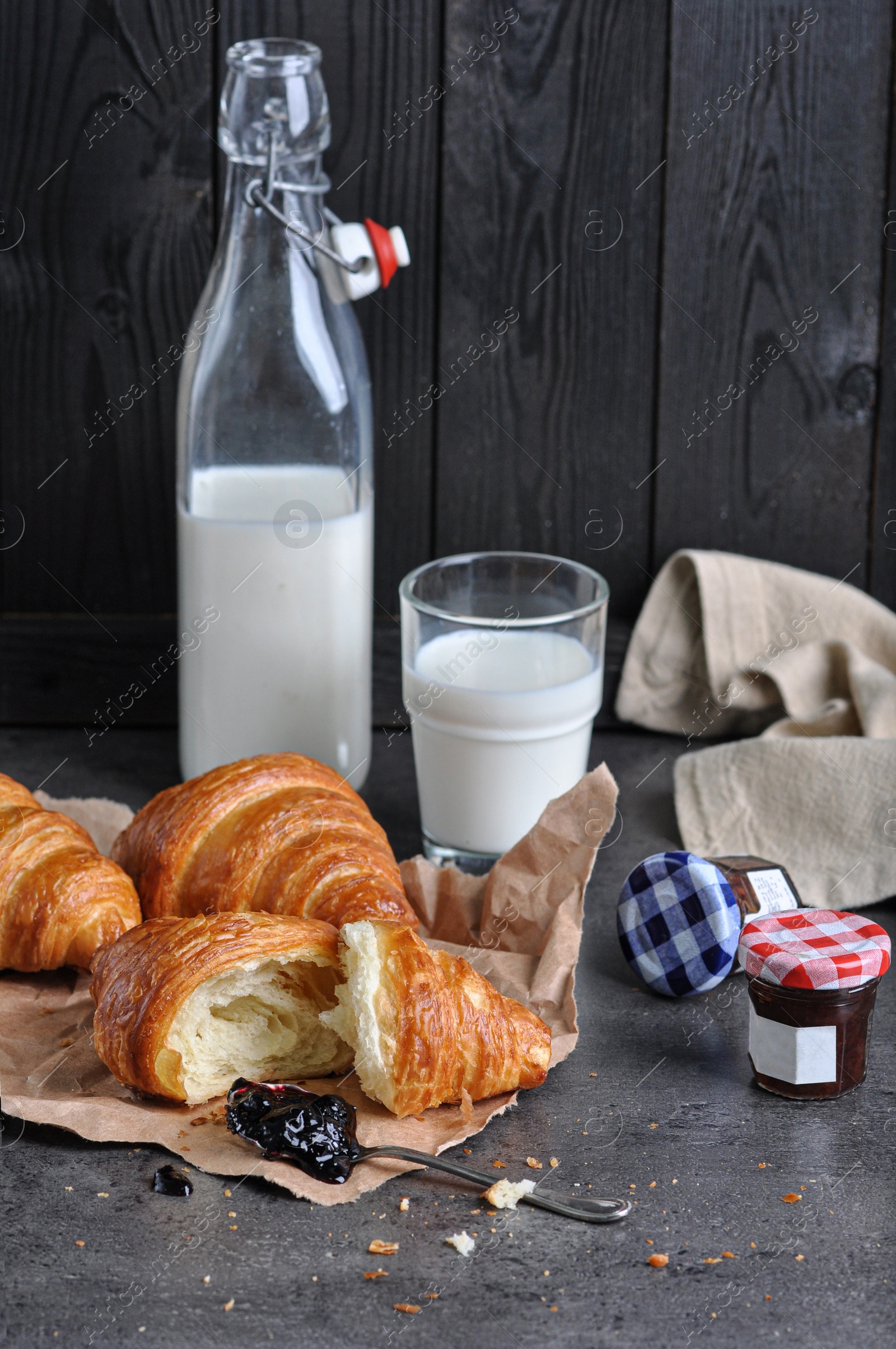 Photo of Tasty fresh croissants with jam and milk on grey table