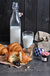 Tasty fresh croissants with jam and milk on grey table