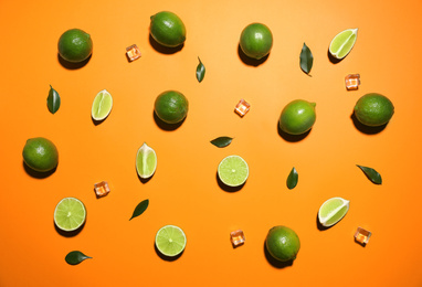 Photo of Flat lay composition with fresh juicy limes and ice cubes on orange background