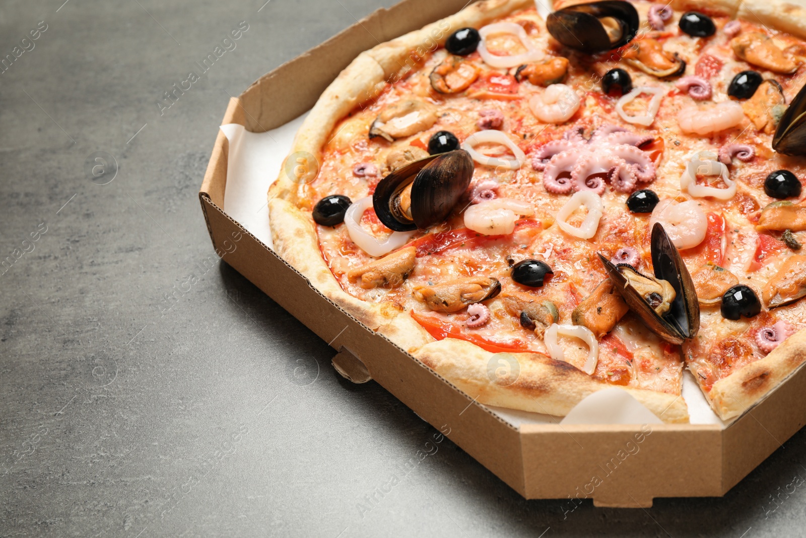 Photo of Delicious seafood pizza in box on grey table, closeup