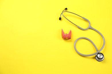 Photo of Endocrinology. Stethoscope and model of thyroid gland on yellow background, top view. Space for text