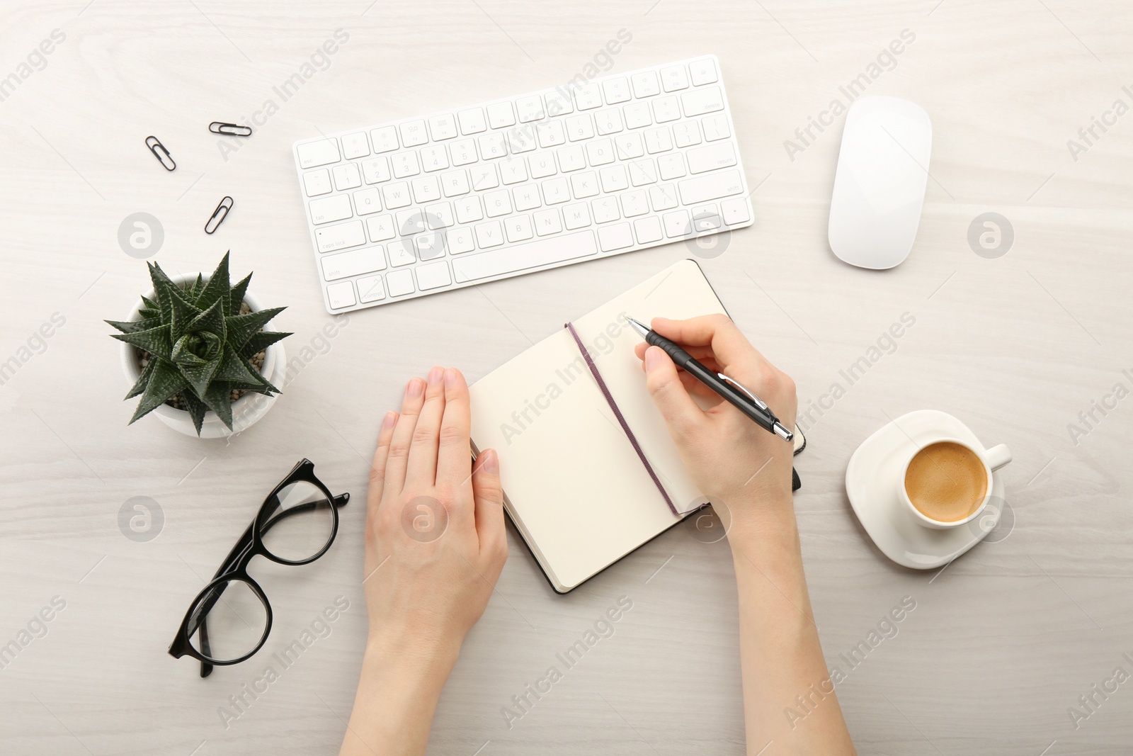 Photo of Woman writing in notebook at light wooden table, top view