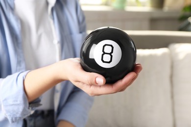 Photo of Woman holding magic eight ball indoors, closeup