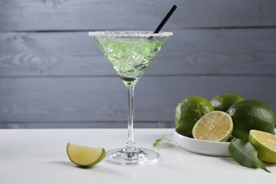 Delicious Margarita cocktail with ice cubes in glass and lime on white table