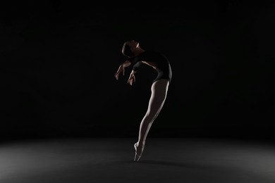 Photo of Young ballerina practicing dance moves on black background