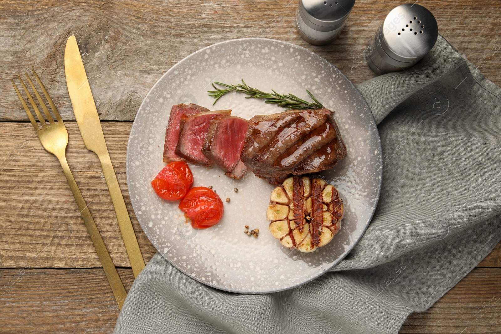 Photo of Delicious grilled beef steak served with spices and tomatoes on wooden table, flat lay