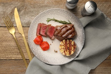 Photo of Delicious grilled beef steak served with spices and tomatoes on wooden table, flat lay