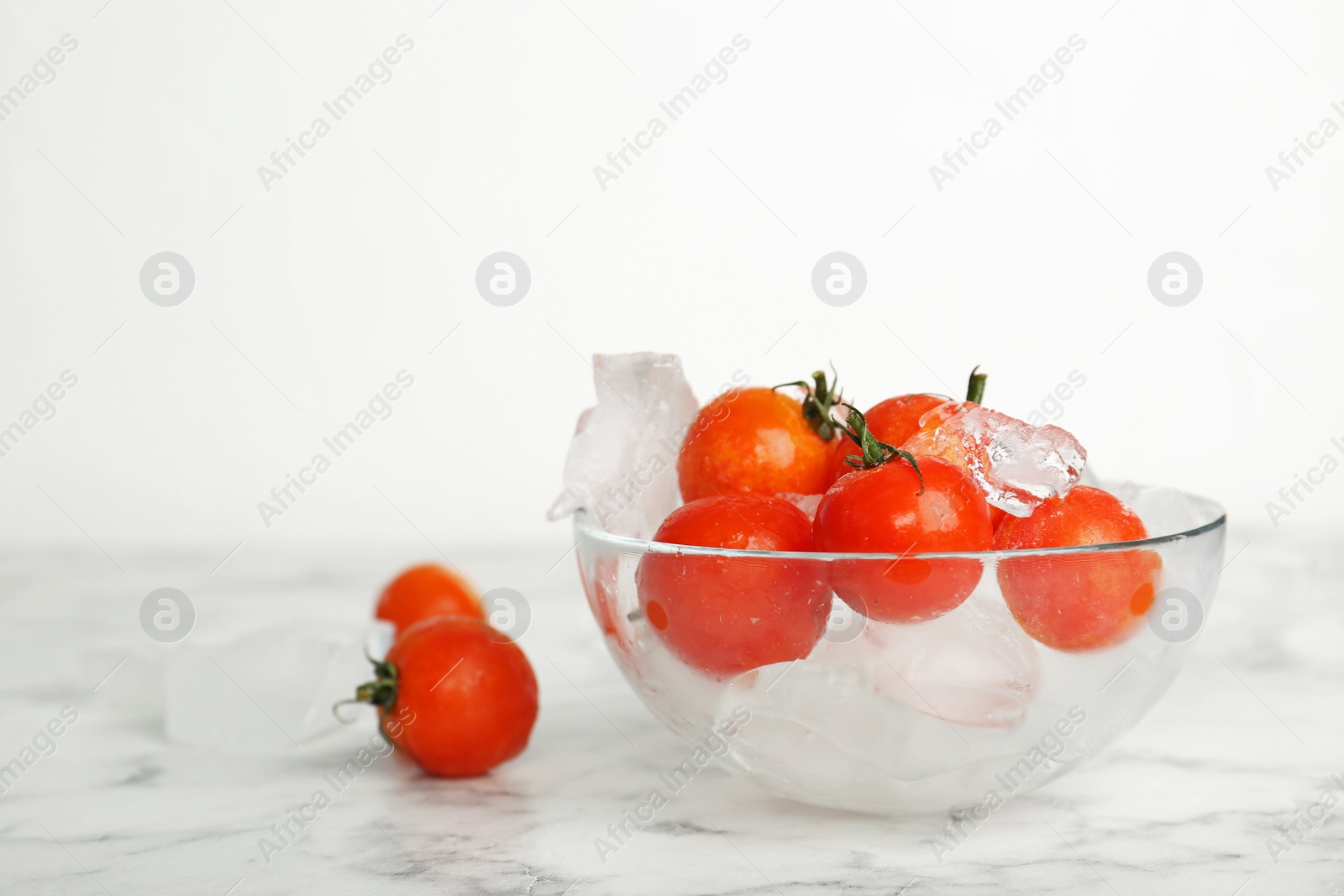 Photo of Bowl with frozen cherry tomatoes and ice cubes on marble table. Keeping vegetables fresh