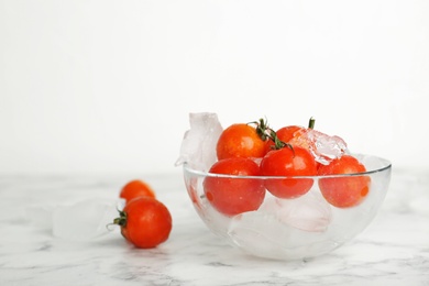 Photo of Bowl with frozen cherry tomatoes and ice cubes on marble table. Keeping vegetables fresh