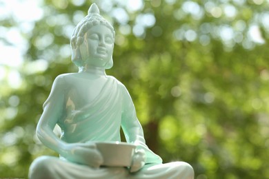 Photo of Beautiful ceramic Buddha sculpture on blurred background, closeup. Space for text