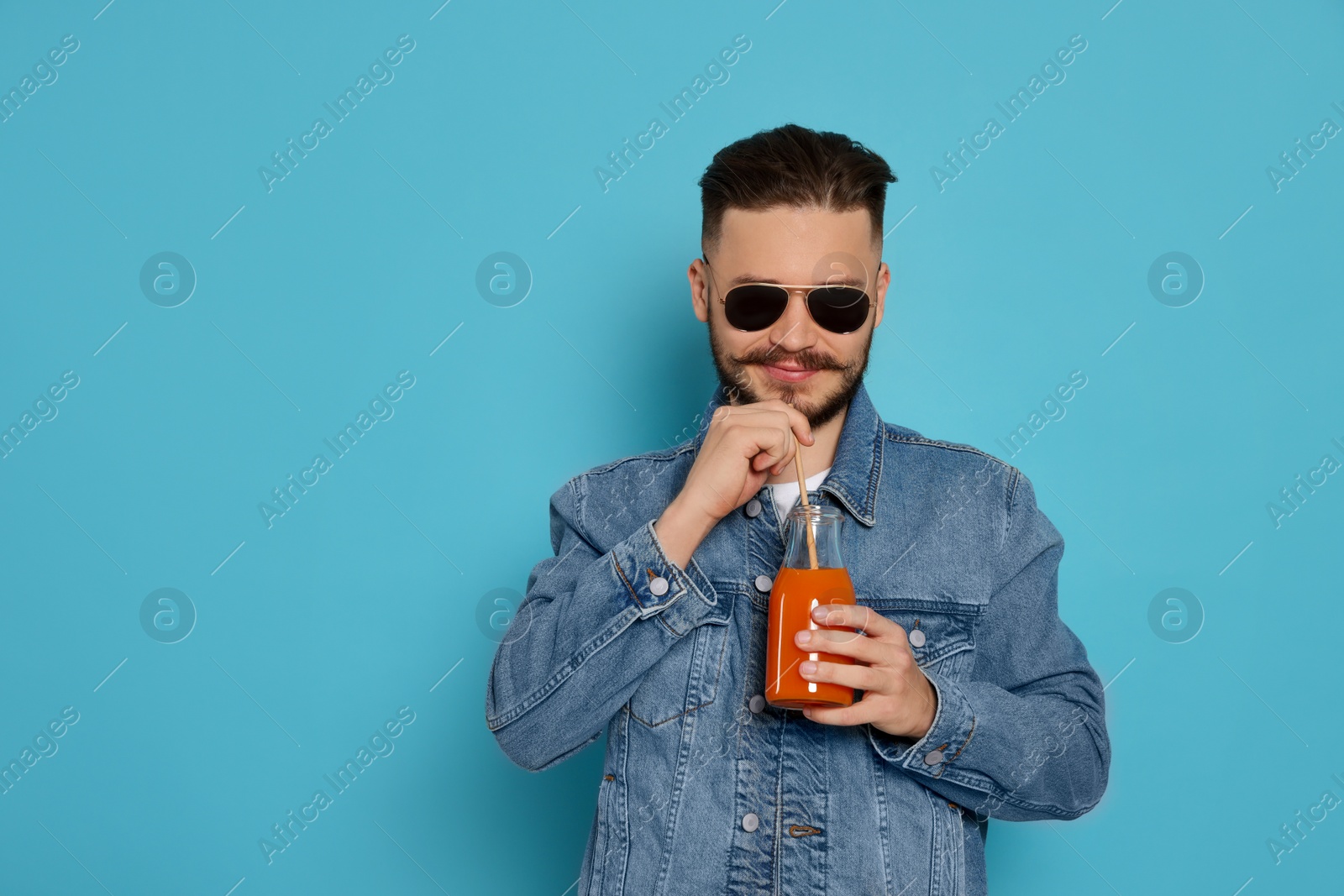 Photo of Handsome young man with glass bottle of juice on light blue background