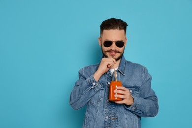 Handsome young man with glass bottle of juice on light blue background