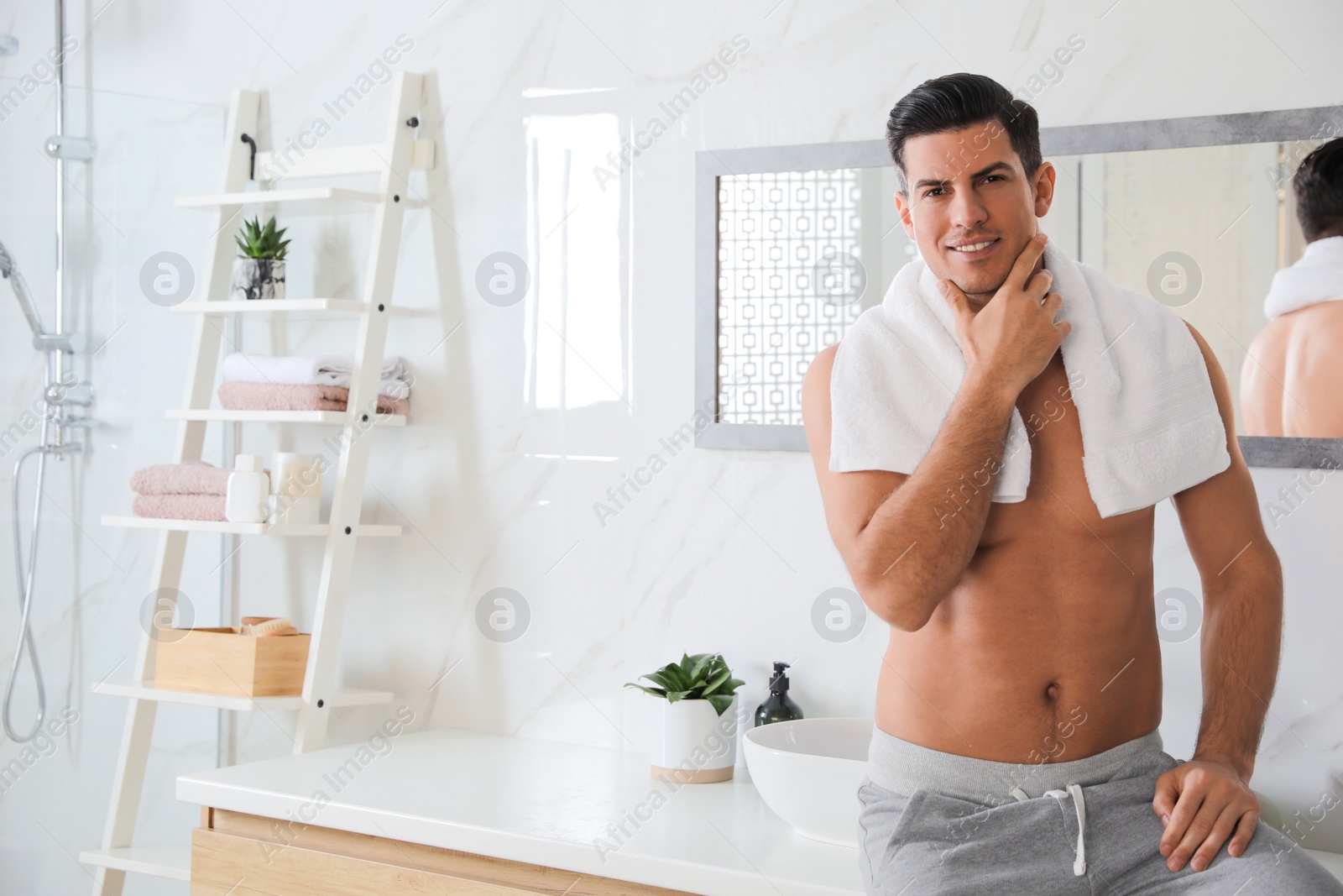 Photo of Handsome man touching his smooth face in bathroom after shaving