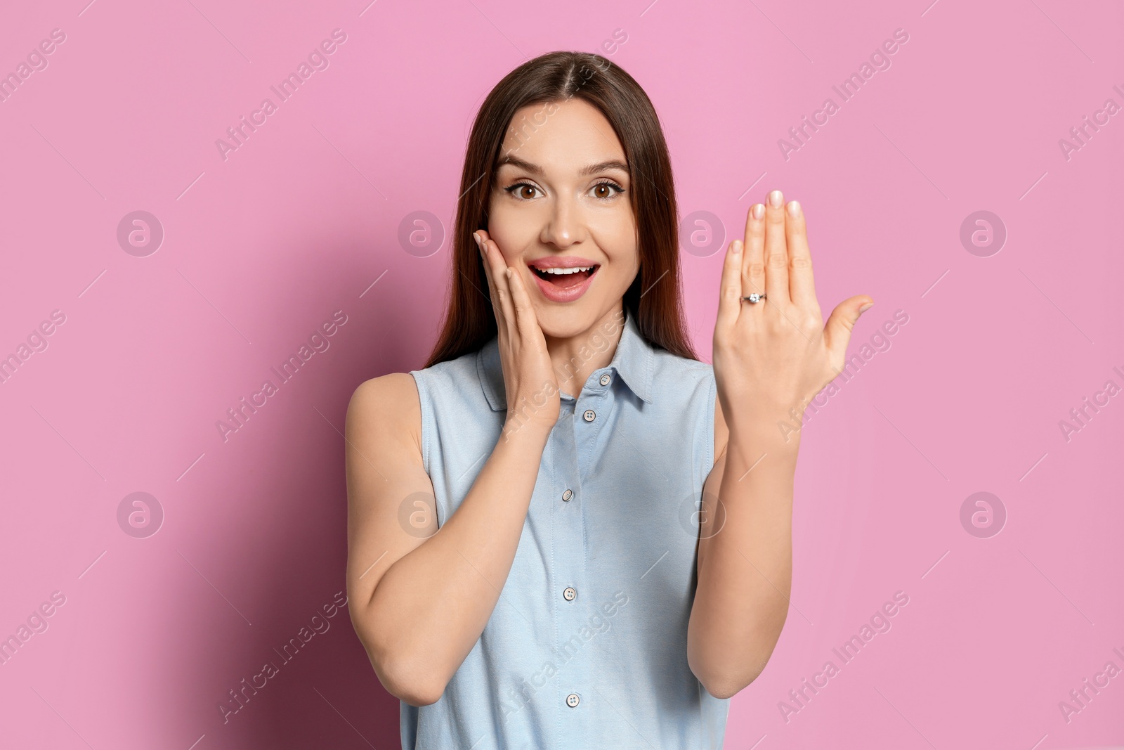 Photo of Happy young woman wearing beautiful engagement ring on pink background