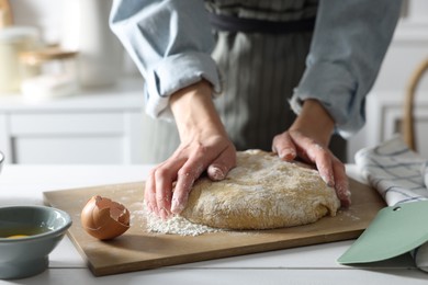 Woman kneading dough at white wooden table in kitchen, closeup