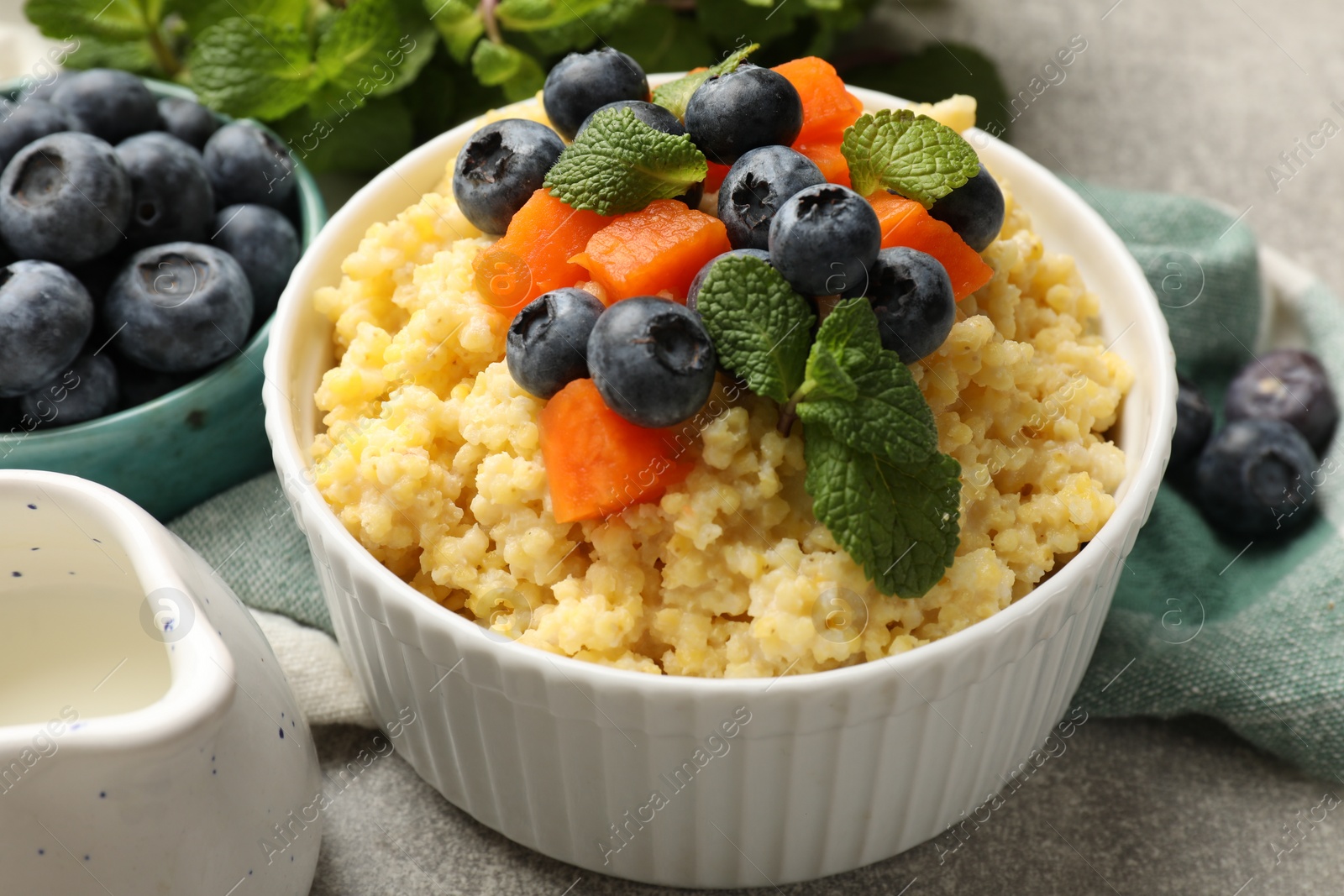 Photo of Tasty millet porridge with blueberries, pumpkin and mint in bowl on light grey table, closeup