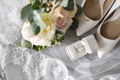 Pair of white high heel shoes, veil, rings and wedding bouquet on grey background, flat lay