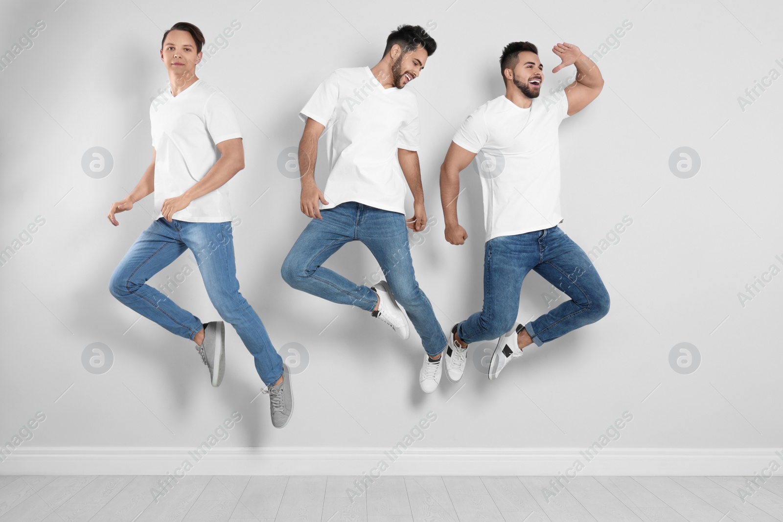 Photo of Group of young men in stylish jeans jumping near light wall