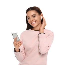 Happy young woman with smartphone listening to music through wireless earphones on white background