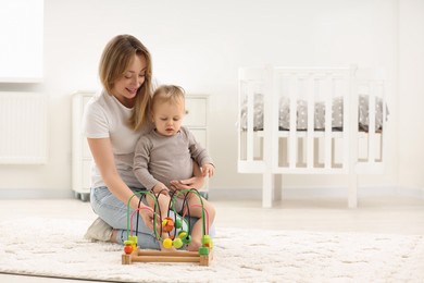 Photo of Children toys. Happy mother and her little son playing with bead maze on rug at home, space for text