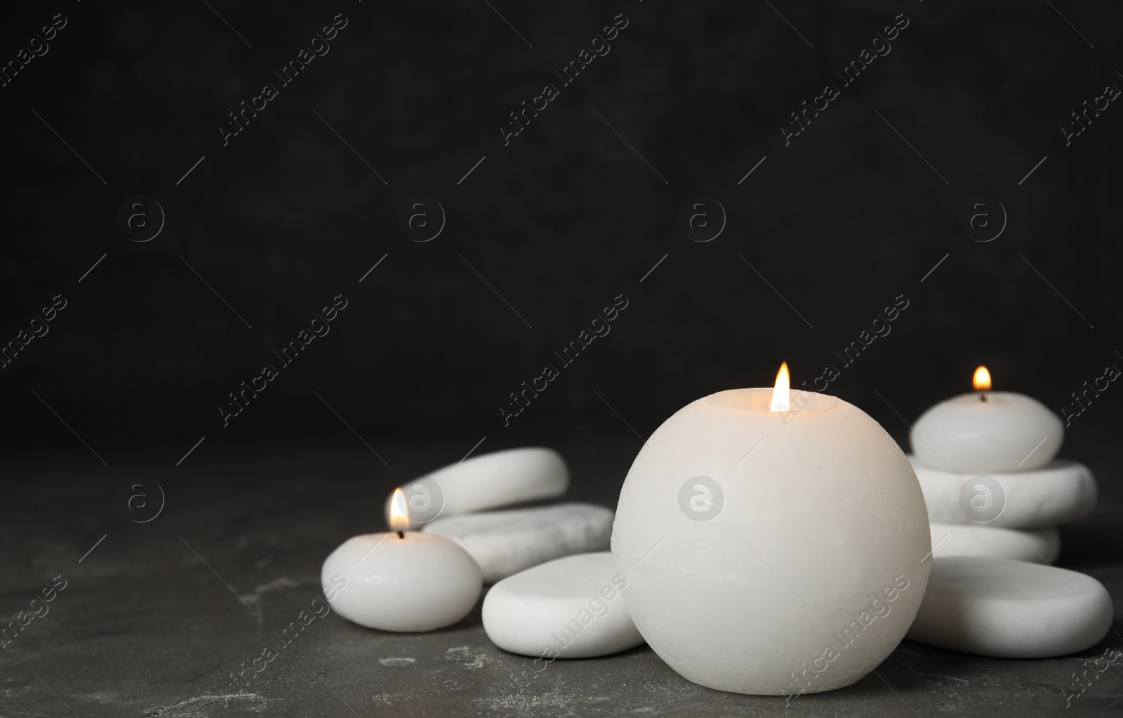 Photo of Burning candles and white spa stones on grey table, space for text