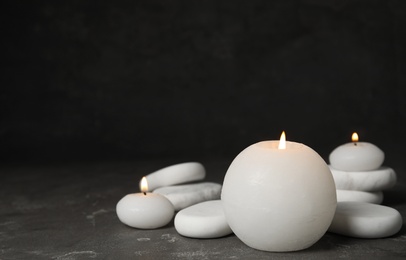 Burning candles and white spa stones on grey table, space for text