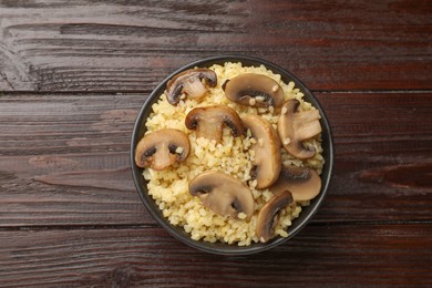 Delicious bulgur with mushrooms in bowl on wooden table, top view